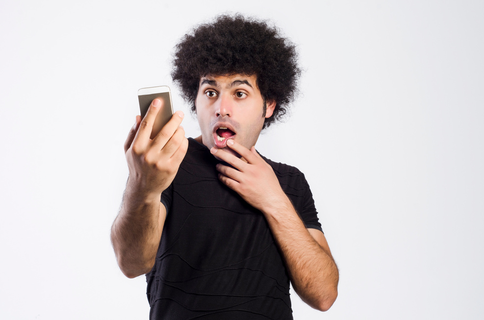 young man on a gray background looks at the phone and is surprised